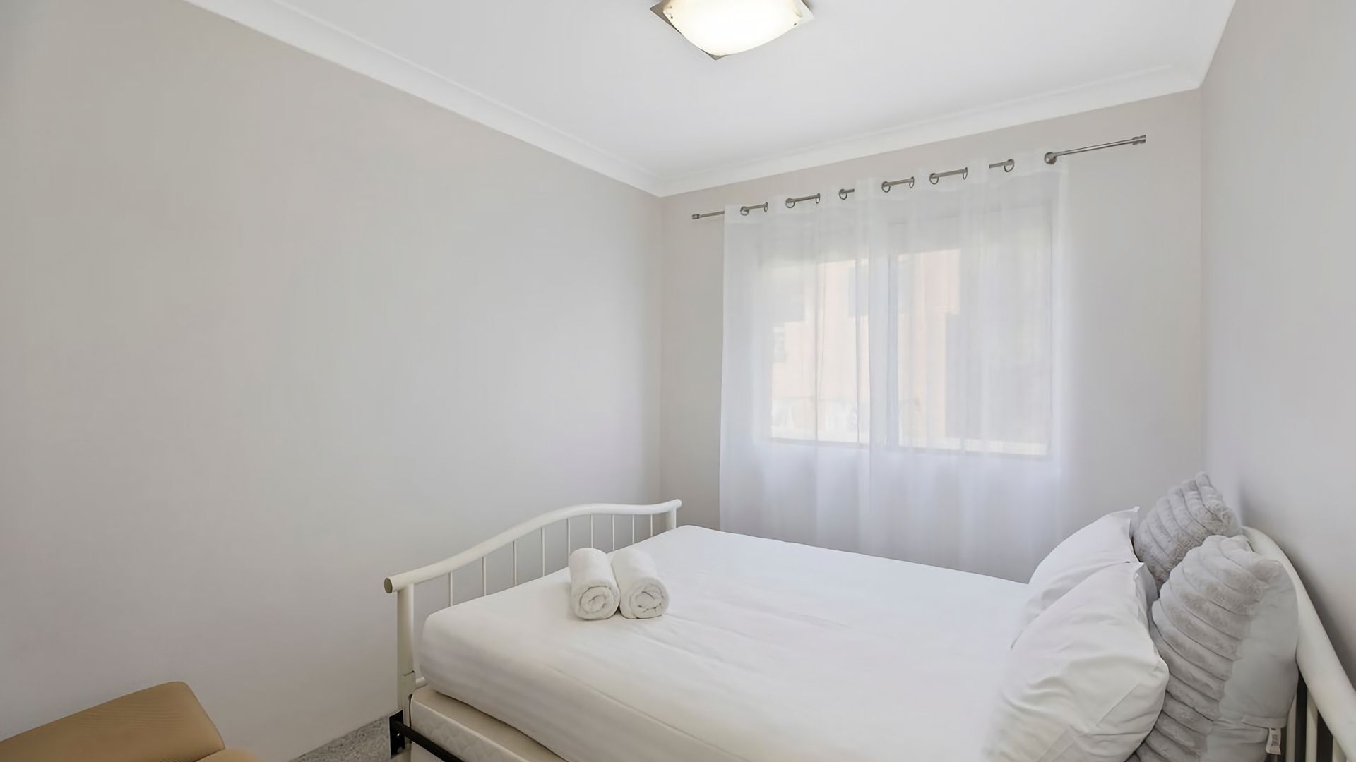 Ein Schlafzimmer mit Bett, Fenster mit leichtem Vorhang und Nachttisch.