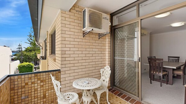 A balcony with a tiled floor, a table with chairs, and a sliding glass door leading to an indoor dining area.
