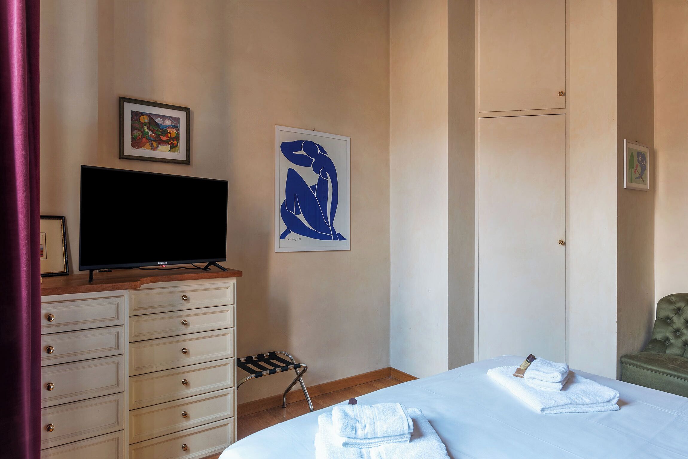 Een hotelkamer met een bed, een televisie op een dressoir, een stoel en kunstwerken aan de wanden.