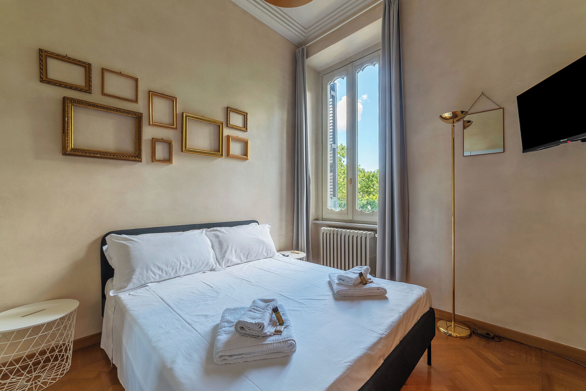 Habitación de hotel con una cama grande, una ventana con cortinas, un televisor de pantalla plana y varios cuadros colgados en la pared.