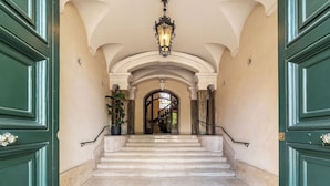 Imponente entrada con una escalera de mármol, puertas verdes y un clásico candelabro.