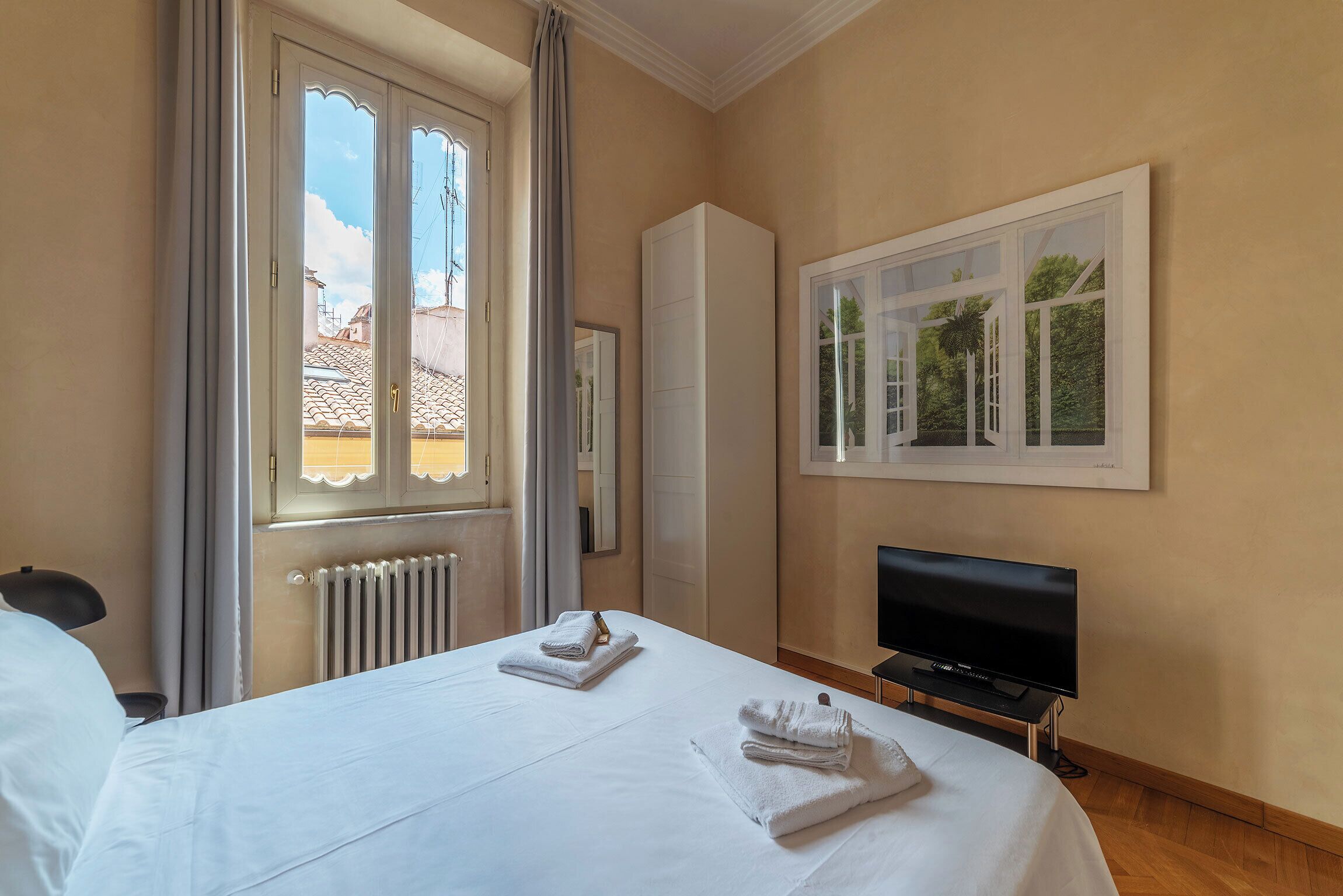 A hotel room with a bed, a TV, and a window with a view of buildings.