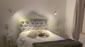 A bedroom with a large bed, a headboard with a circular pattern, bedside lamps, a fluffy throw blanket, and a striped bench. - Charming single-storey house with saltwater pool. Completely renovated in 2022 (Espéraza)