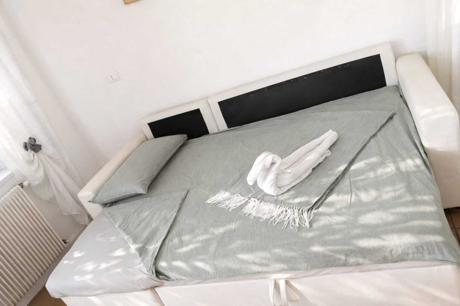 A bed with a grey blanket, pillows, and a white towel.