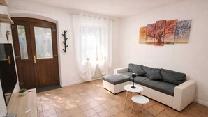Un salon avec un canapé, une petite table d’appoint, une porte et une fenêtre avec des rideaux.