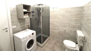Une salle de bain moderne avec une douche à parois de verre, un lave-linge encastré et des toilettes.