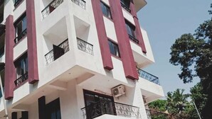 A multi-story building with a white facade and red accents, featuring balconies and a gated entrance. - Rihan Goa Holiday Homes (Calangute)