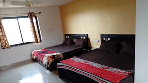 A bedroom with two beds, a ceiling fan, a window with curtains, and a plain wall. - Rihan Goa Holiday Homes (Calangute)