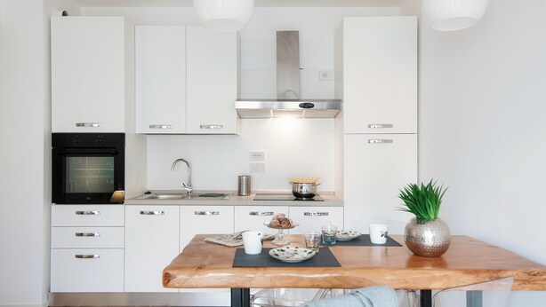 A modern kitchen with white cabinetry, stainless steel appliances, and a wooden dining table. - Cozy JOIVY Suite 3 with parking (Como)