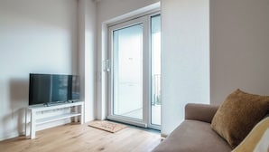 A modern living room with a flat-screen TV on a white stand, a sliding glass door leading to a balcony, and a beige sofa with a brown cushion. - Cozy JOIVY Suite 3 with parking (Como)