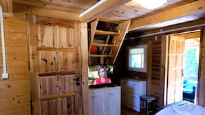 A wooden cabin interior with a kitchen area, a bed, and a window. - Cottage in Dziwnow Near the Beach (Dziwnów)