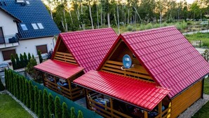 Two wooden cabins with red roofs, each featuring a balcony and a small porch area. - Cottage in Dziwnow Near the Beach (Dziwnów)