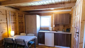 A compact kitchen with wooden cabinets, a dining table with chairs, and a window providing natural light. - Cottage in Dziwnow Near the Beach (Dziwnów)