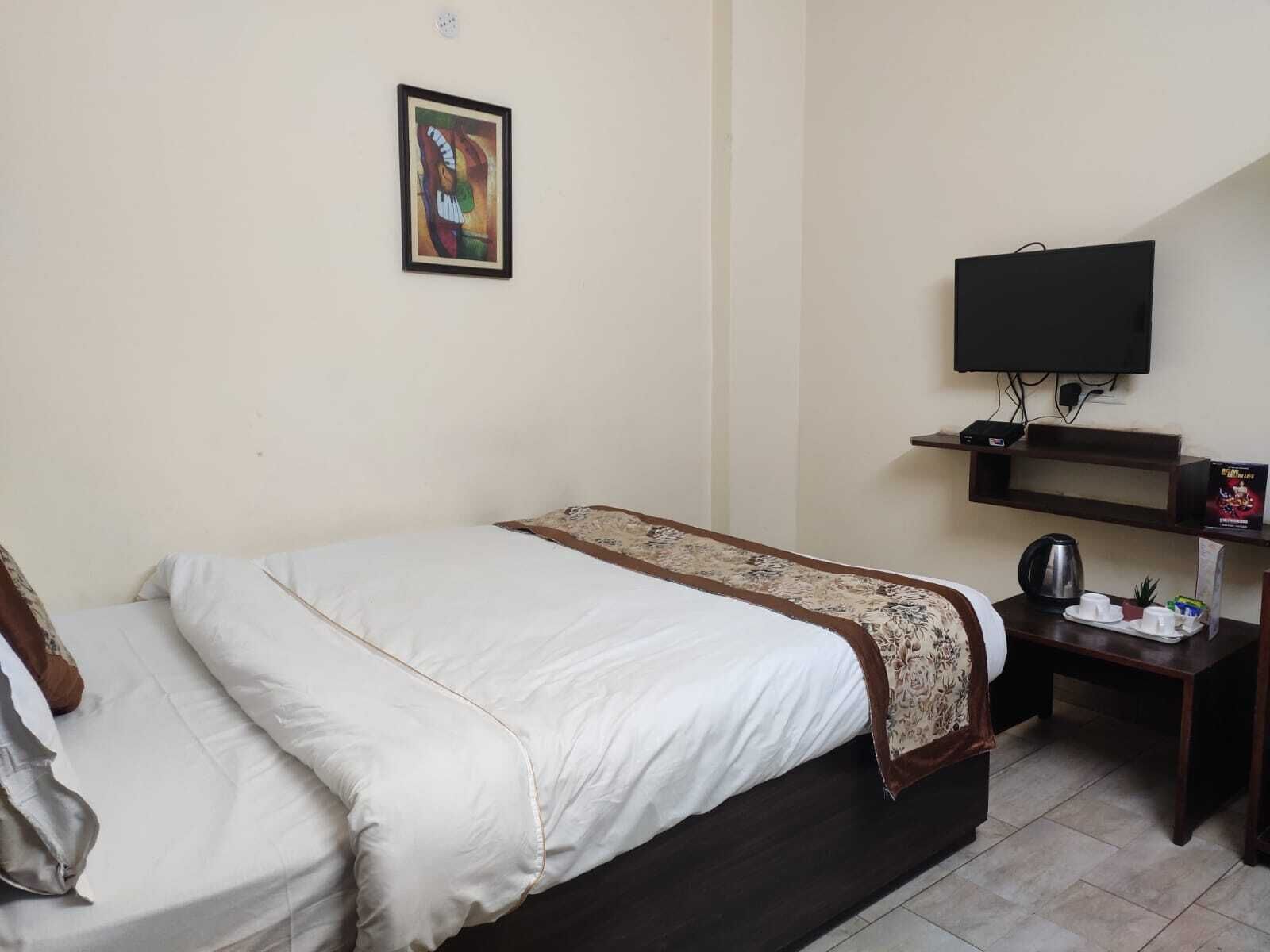 Een hotelkamer met een bed, een televisie, een klein tafeltje met een waterkoker en een ingelijst schilderij aan de muur.