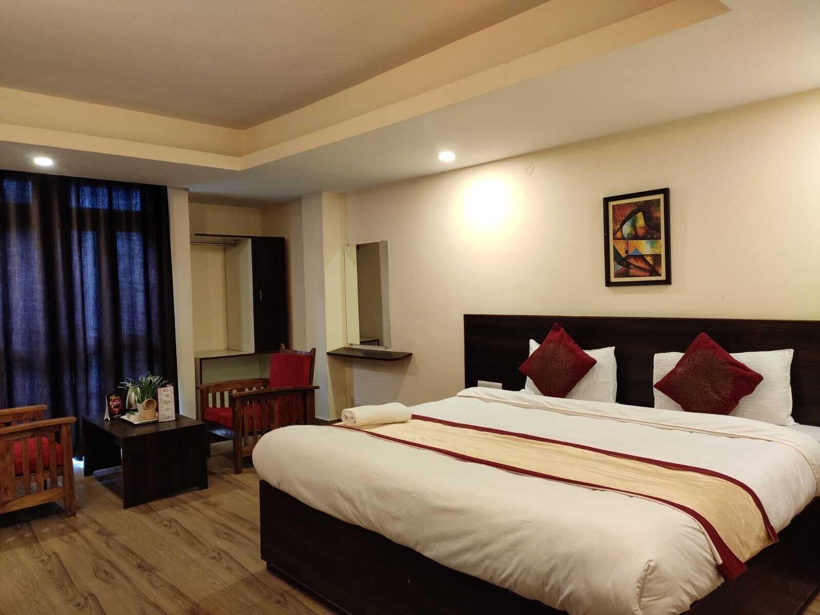 A hotel room with a large bed, a desk, a chair, a mirror, and a painting on the wall.