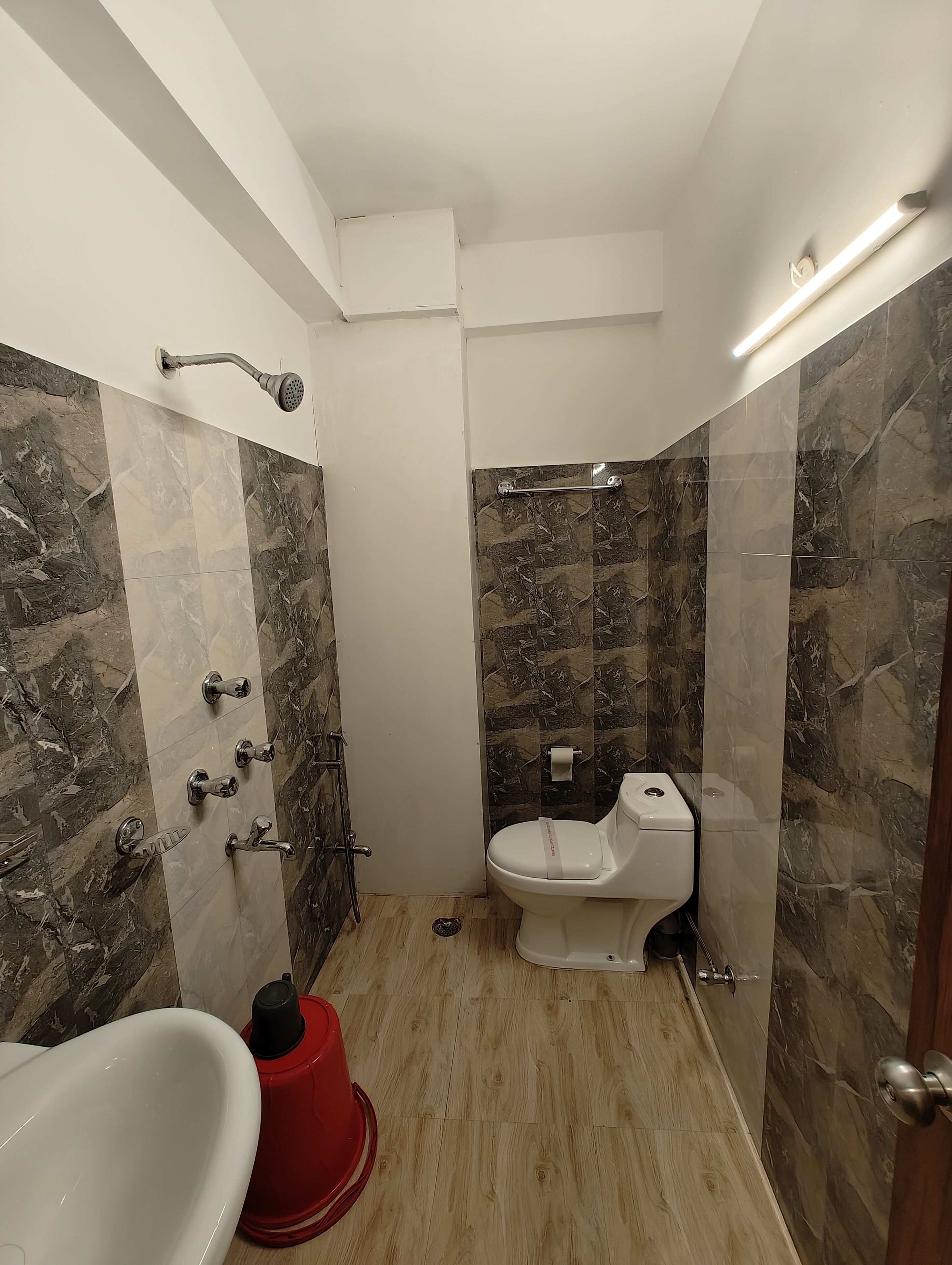 A compact bathroom with a shower, toilet, and a red bucket.