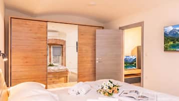 A hotel room with a bed, a wooden wardrobe, a mirror, and a painting of a mountain landscape.