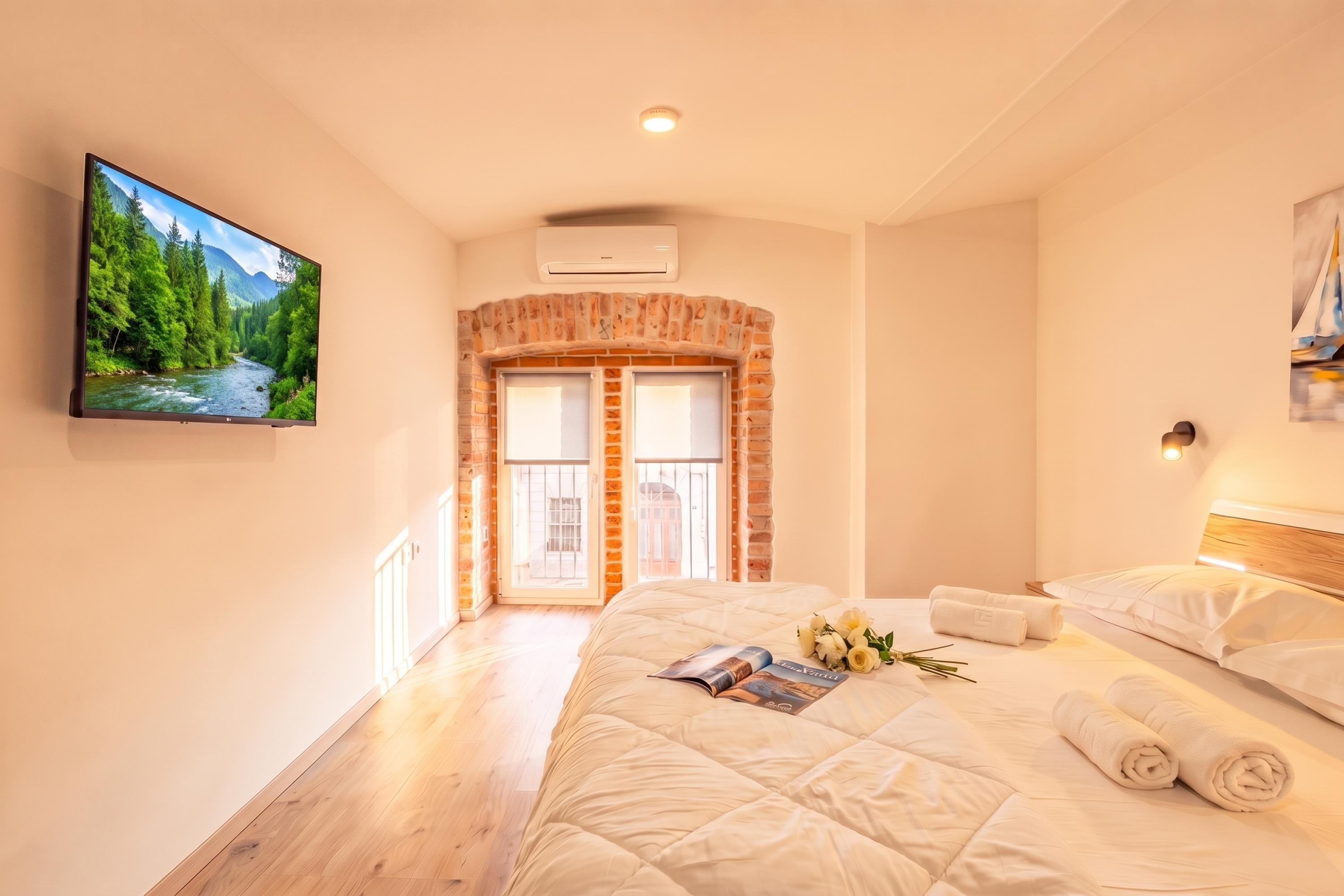 Een hotelkamer met een bed, een televisie, een bakstenen openhaard en uitzicht op een bos.