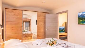 A hotel room with a bed, a wooden wardrobe, a mirror, and a painting of a mountain landscape.