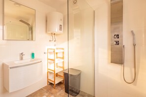 A modern bathroom with a glass-enclosed shower, a white sink with a mirror, and a wooden shelf unit. - Rijeka City Vibes Apartment (Rijeka)