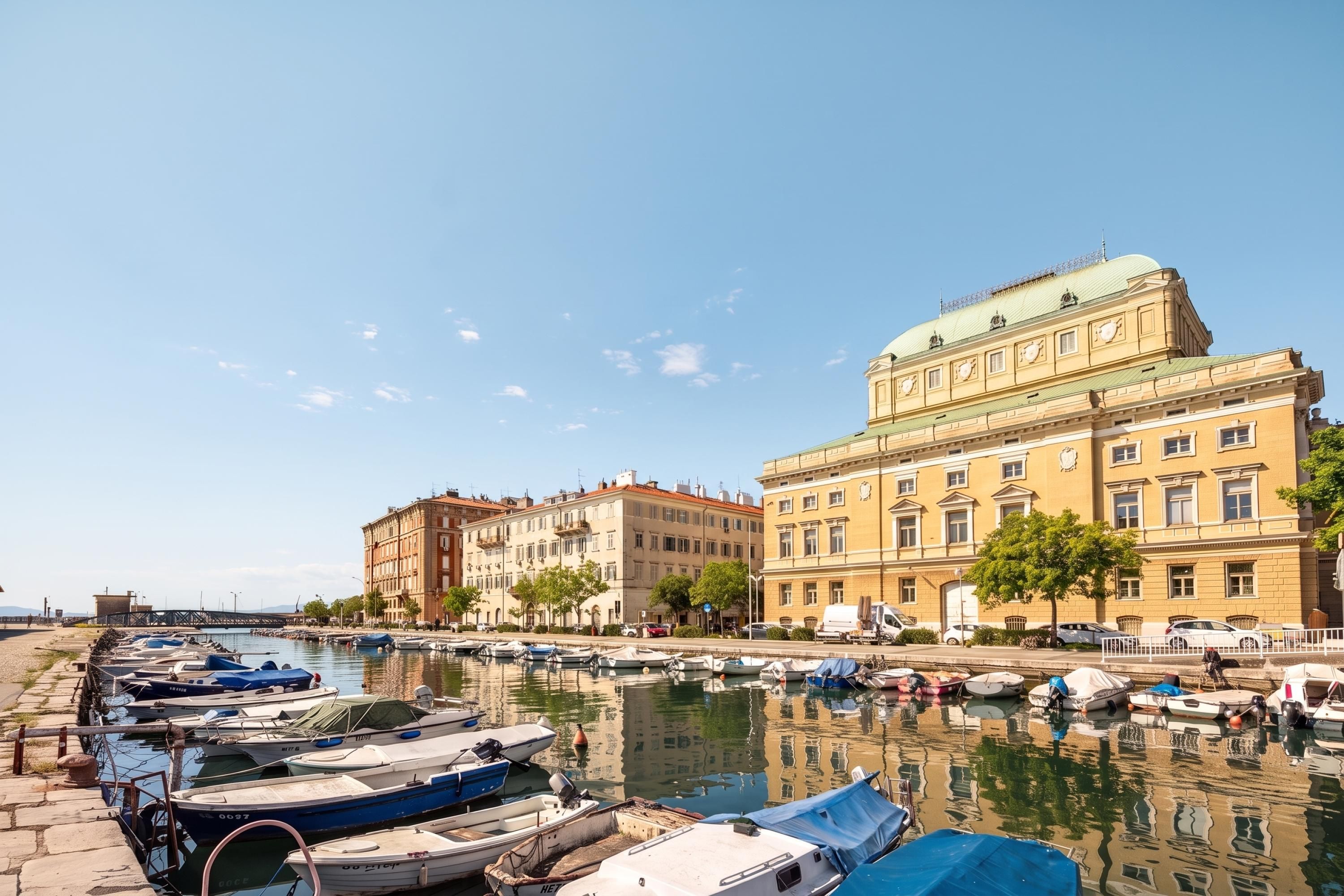 A marina with boats docked, a large building with classical architecture, and a clear sky.