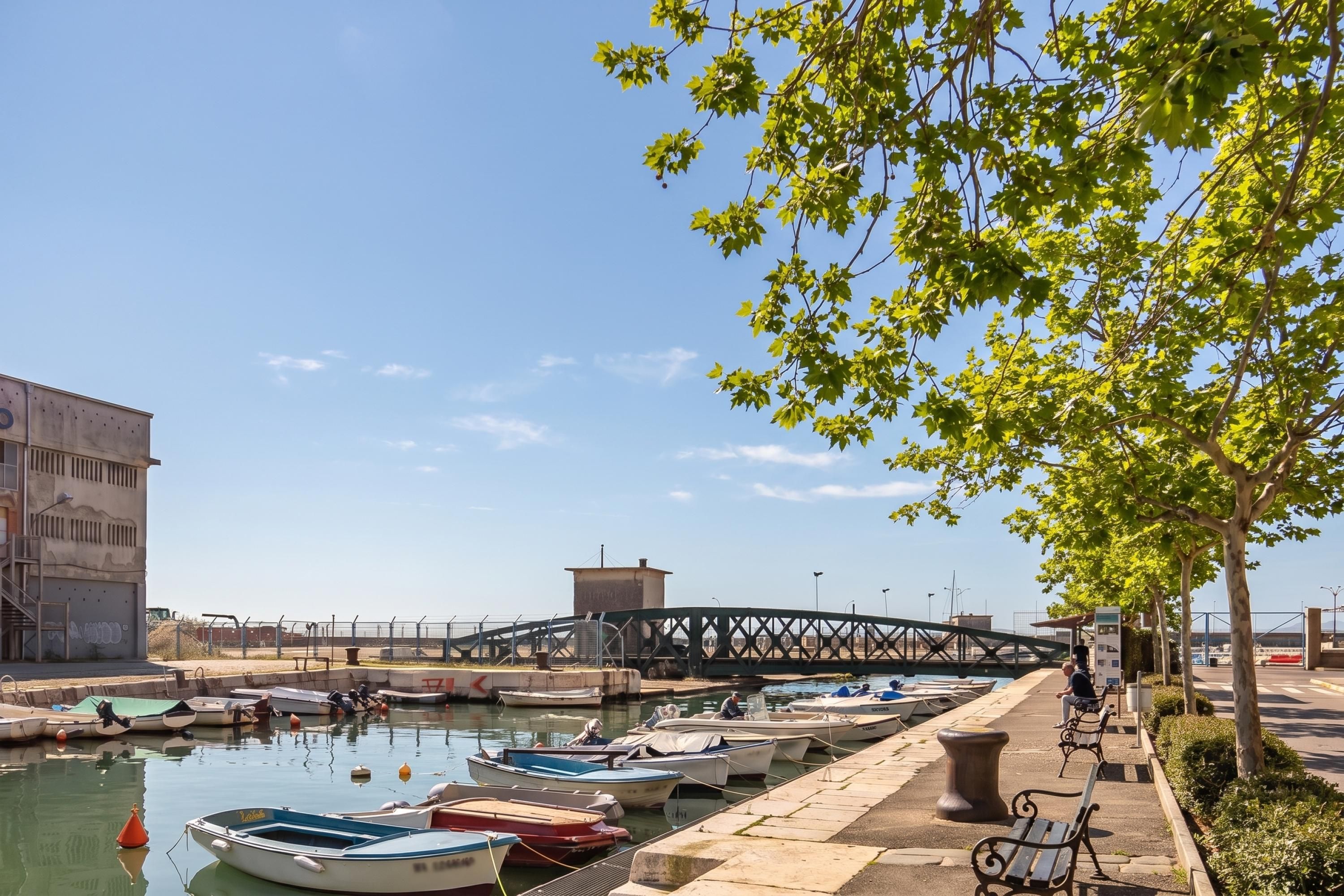 A marina with boats docked, a pedestrian walkway, and a bridge in the background.