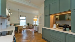 Een moderne keuken met blauwgroene kastjes, een houten visgraatvloer en een eethoek met uitzicht op zee.