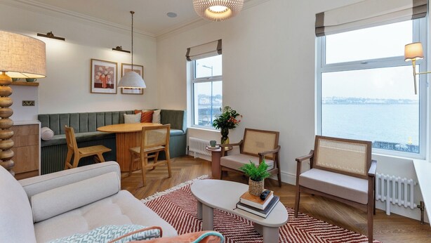 Een gezellige woonkamer met een groene bank, een houten salontafel en uitzicht op een waterpartij door grote ramen.