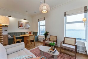 A cozy living room with a green sofa, wooden coffee table, and a view of a body of water through large windows. - Modern 2-bed Apartment - Sleeps 6 - Seafront View (Donaghadee)