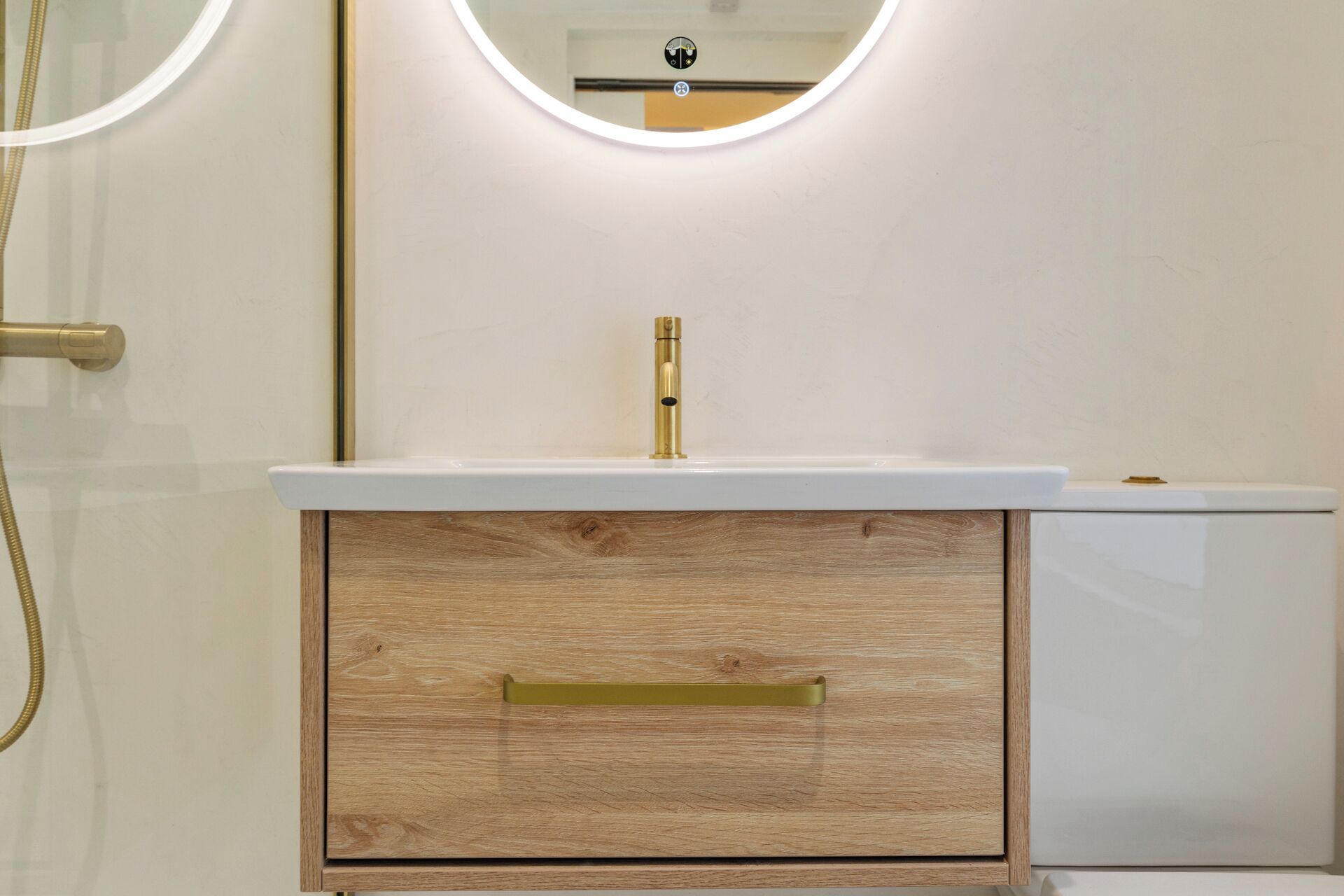A bathroom with a wooden vanity, a white sink, and a gold faucet.