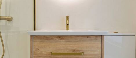 A bathroom with a wooden vanity, a white sink, and a gold faucet.
