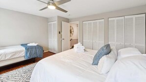 Een slaapkamer met een bed, een bijzetbed, een plafondventilator en witte kasten.