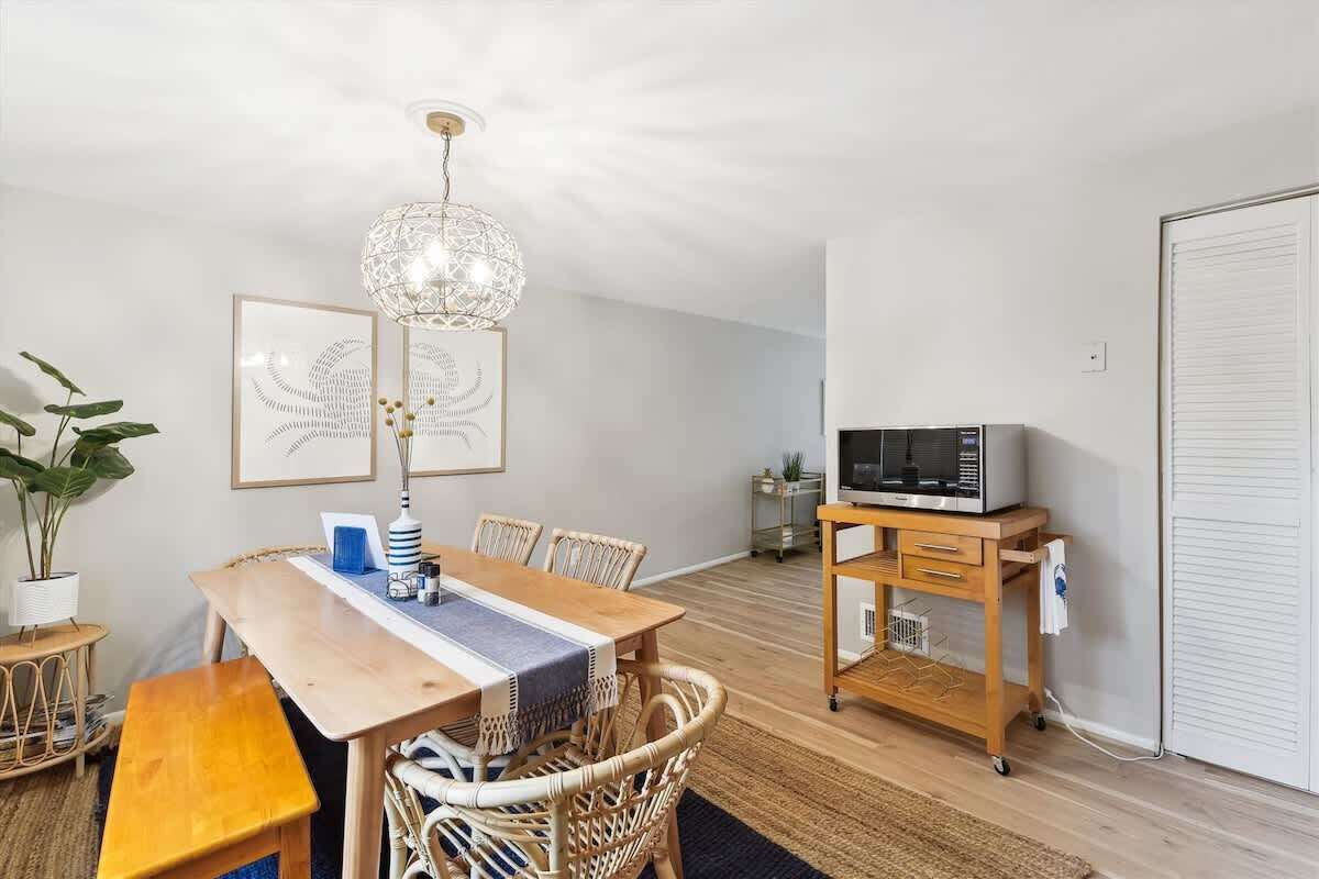 A dining area with a wooden table, wicker chairs, a hanging light fixture, and a microwave on a cart.