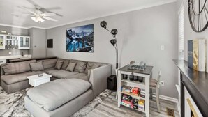 Una sala moderna con un sofá modular, una mesita blanca, una estantería y un cuadro grande de un paisaje nevado.