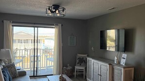 A living room with a sofa, coffee table, and TV. There is a sliding glass door leading to an outdoor area with a view of a house and a fence.
