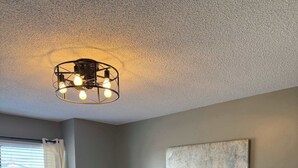 A bedroom with a bed, a nightstand, a lamp, a ceiling light fixture, and a window with curtains.