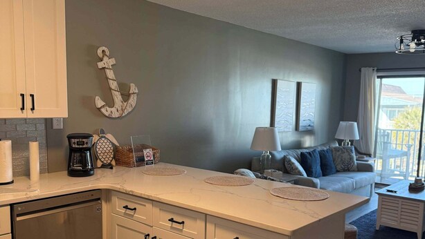 A modern kitchen with white cabinets, a built-in dishwasher, and a central island with a coffee maker and decorative items.