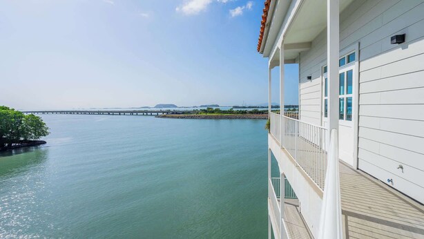 Ein Ufergrundstück mit einem Balkon mit Blick auf ruhiges Wasser, eine entfernte Brücke und einen klaren Himmel.