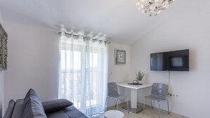 A modern living room with a grey sofa, a dining area with two chairs, a small table, and a TV mounted on the wall. - Dolce Vita Apartment 3 with Heated Pool near Poreč (Mugeba)