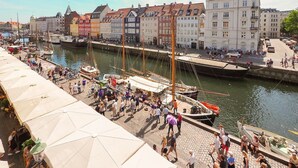 A bustling riverside promenade with a row of colorful buildings, a dock with boats, and a crowd of people. - Charming Nyhavn Apartment - Stunning Canal Views (København)