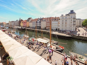 Eine belebte Uferpromenade mit einer Reihe bunter Gebäude, einem Steg mit Booten und einer Menschenmenge.