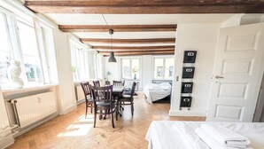 A room with a wooden floor, a bed with white bedding, a dining table with chairs, and a radiator. - Charming Nyhavn Apartment - Stunning Canal Views (København)
