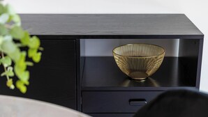 Un módulo de almacenamiento negro con un bol de borde dorado encima.