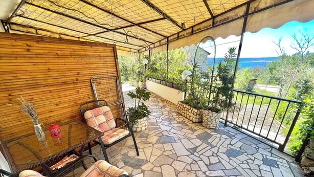 A covered patio with stone flooring, two wicker chairs, a small table, and potted plants. - Apartment Zeleni Raj 1 (Crikvenica)