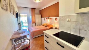 A compact hotel room with a bed, a kitchenette, a dining area, and a bathroom. - Apartment Zeleni Raj 1 (Crikvenica)