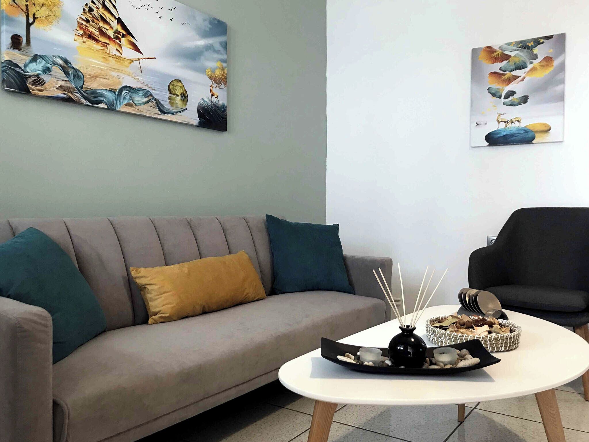 A living room with a grey sofa, a white coffee table with decorative items, and two paintings on the wall.