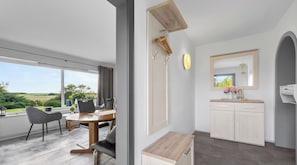 Ein modernes Interieur mit Essbereich, einer Küche mit weißen Schränken und einem großen Fenster mit Blick ins Freie.