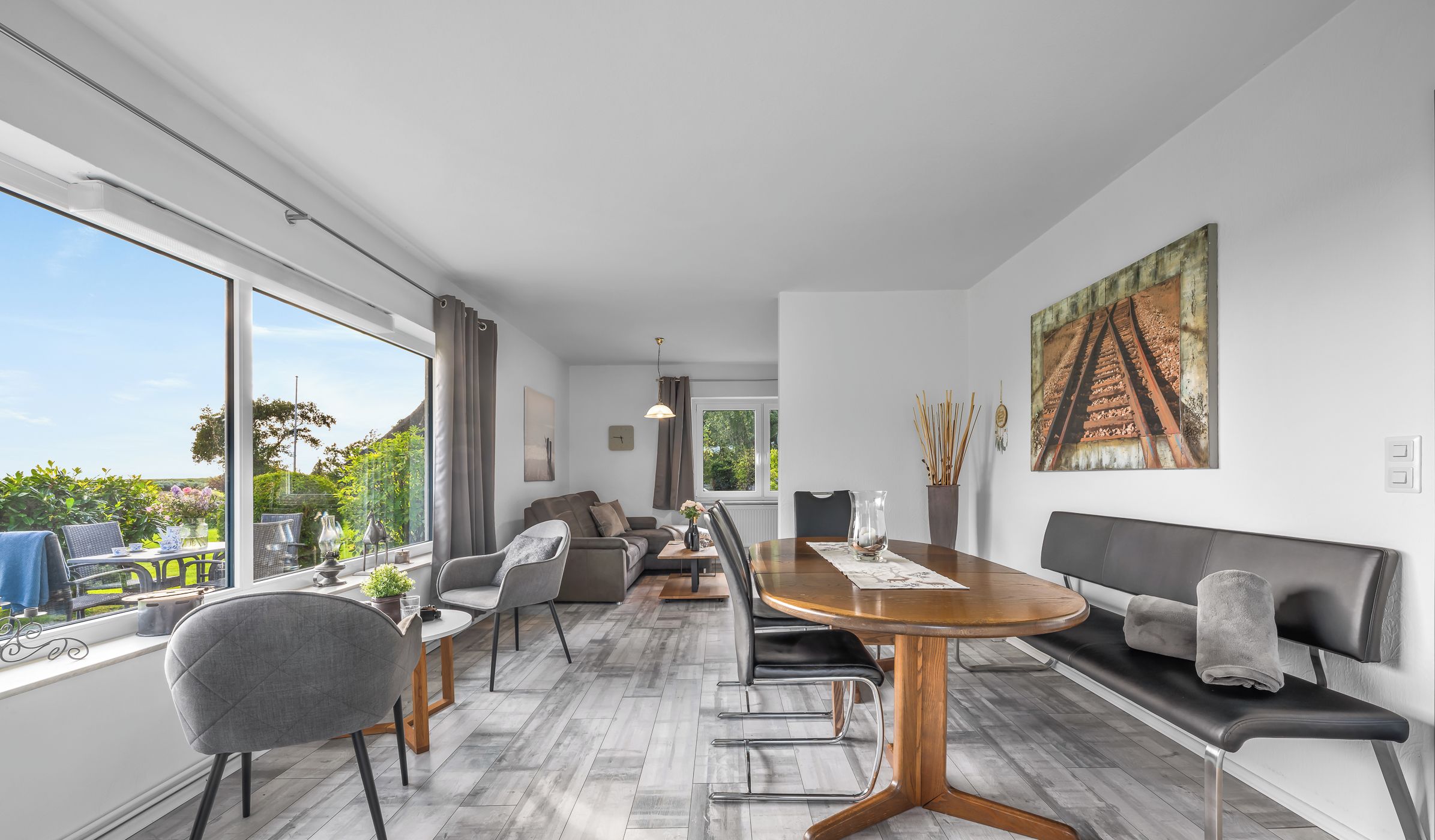 A modern living room with a dining area, large windows, and a view of greenery.