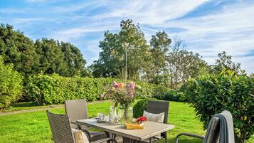 An outdoor dining area with wicker furniture, a table with a vase of flowers, and a view of a lush garden.