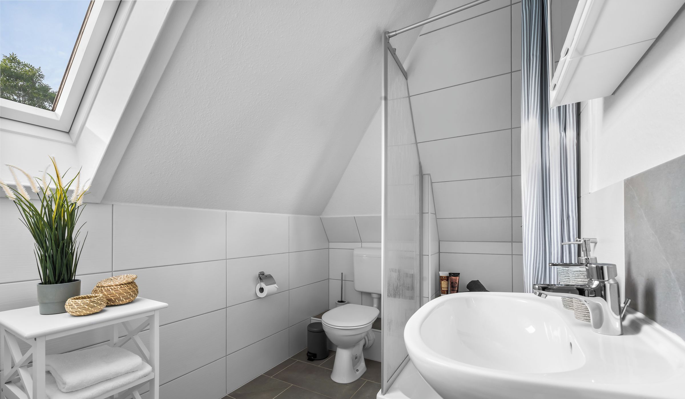 A modern bathroom with a skylight, white tiles, a large sink, and a toilet.